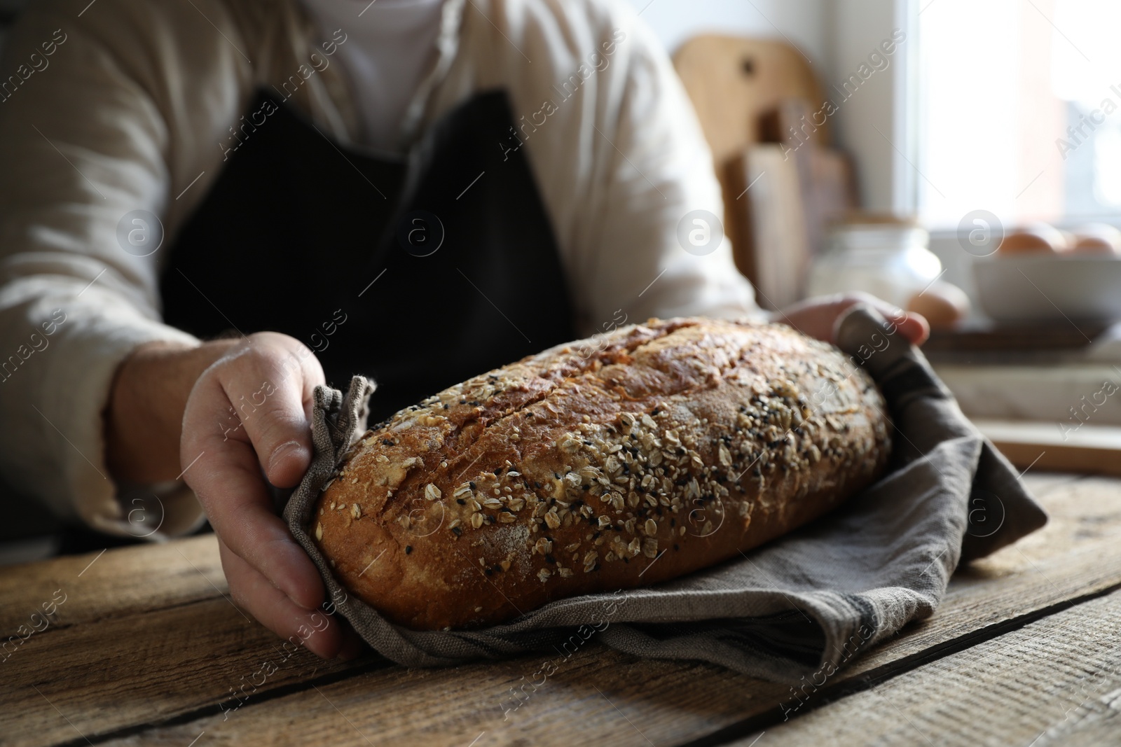 Photo of Man holding loaf of fresh bread at wooden table indoors, closeup