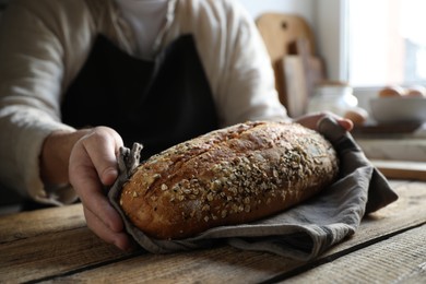 Photo of Man holding loaf of fresh bread at wooden table indoors, closeup