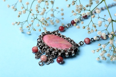 Photo of Beautiful silver necklace with rhodonite and tourmaline gemstones on light blue background
