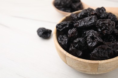Photo of Sweet dried prunes in bowl on white wooden table, closeup. Space for text
