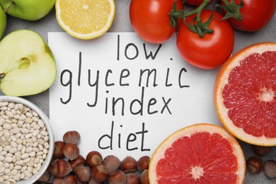 Paper with words Low Glycemic Index Diet and food on grey table, flat lay