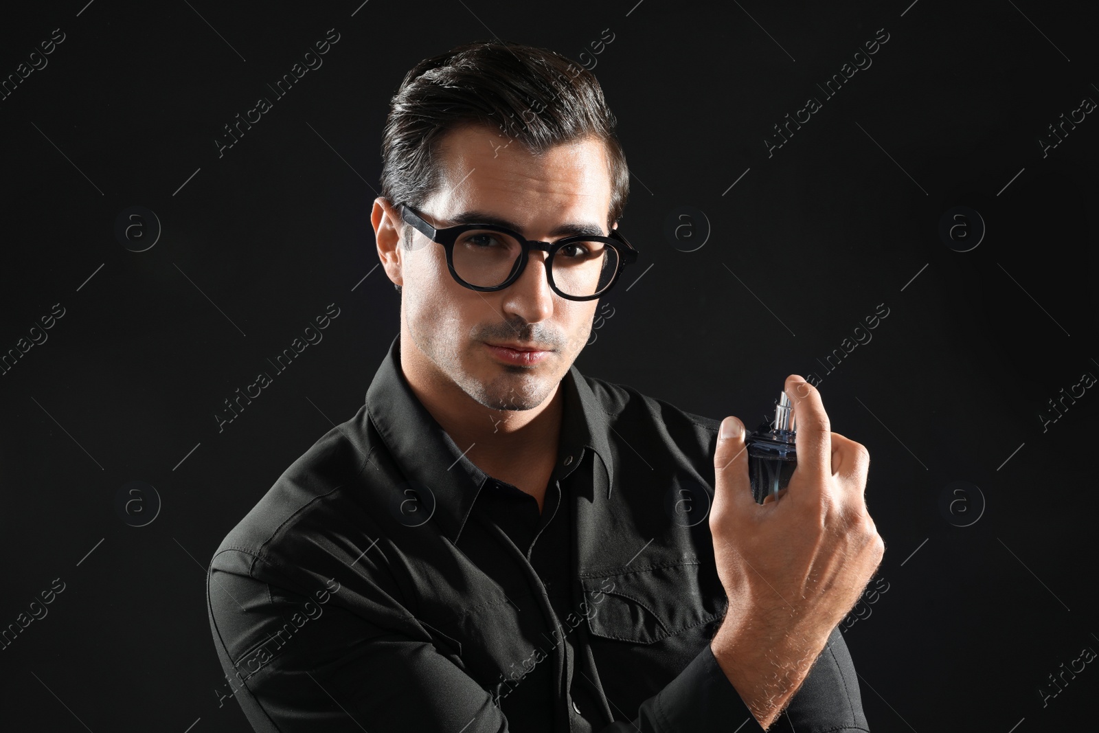 Photo of Handsome young man in glasses with using perfume on black background