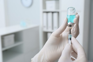 Doctor filling syringe with medication from vial in hospital, closeup