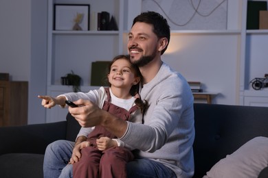 Photo of Father and daughter spending time near TV at home. Happy man holding remote control