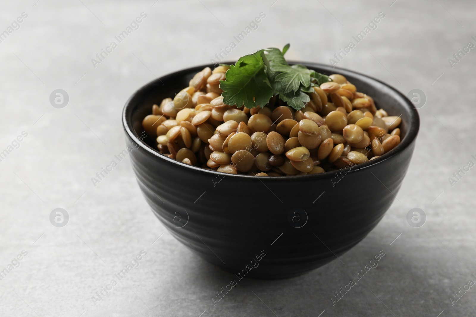 Photo of Delicious lentils with parsley in bowl on light grey table, closeup