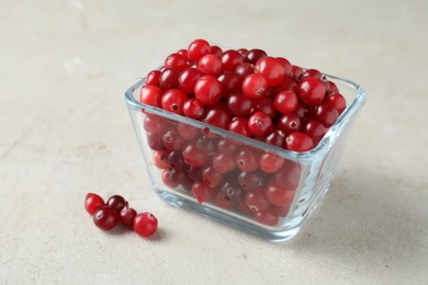 Photo of Cranberries in bowl on light grey table, closeup