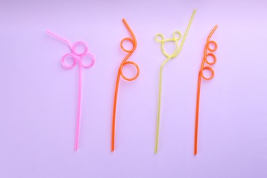 Colorful plastic drinking straws on violet background, flat lay