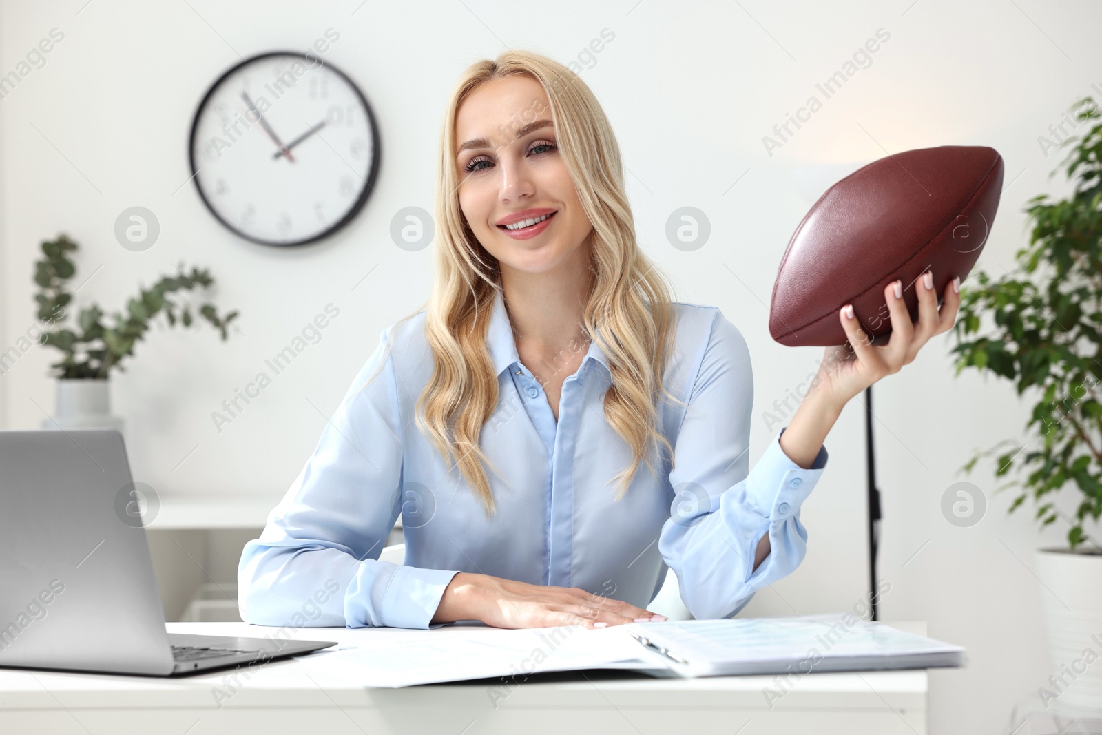 Photo of Happy woman with american football ball at table in office