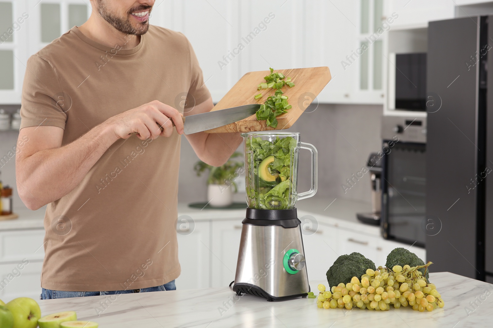 Photo of Man adding cut spinach for delicious smoothie in kitchen, closeup