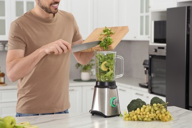 Man adding cut spinach for delicious smoothie in kitchen, closeup