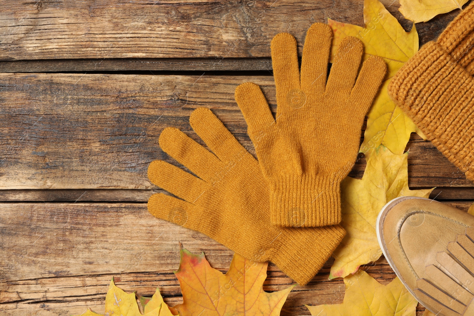 Photo of Flat lay composition with stylish woolen gloves and dry leaves on wooden table. Space for text