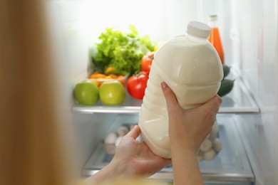Photo of Young woman putting gallon of milk into refrigerator indoors, closeup