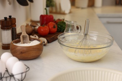 Photo of Metal whisk, cream in bowl and different products on light table indoors