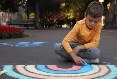 Photo of Child drawing rainbow with chalk on asphalt