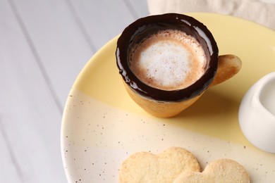 Delicious edible biscuit cup with coffee, milk and heart shaped cookies on white table