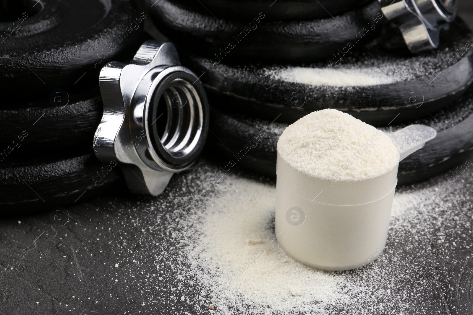 Photo of Measuring scoop of protein powder and weight plates on grey table, closeup