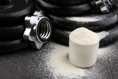 Measuring scoop of protein powder and weight plates on grey table, closeup