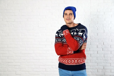 Photo of Portrait of young man in Christmas sweater and hat near white brick wall. Space for text