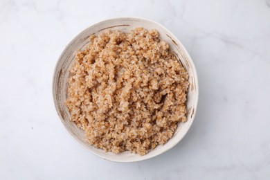 Photo of Tasty wheat porridge in bowl on white marble table, top view