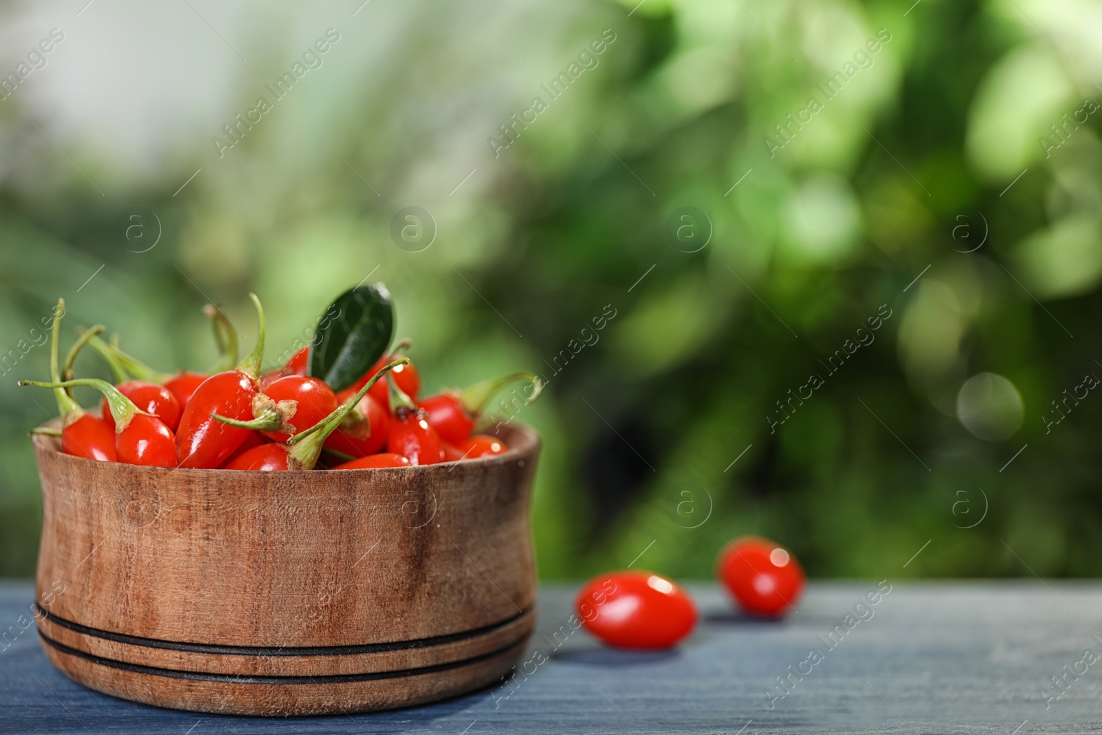 Photo of Bowl with fresh goji berries on blue wooden table against blurred background. Space for text