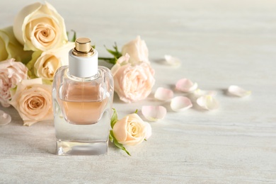 Photo of Elegant bottle of perfume and flowers on light stone background, space for text