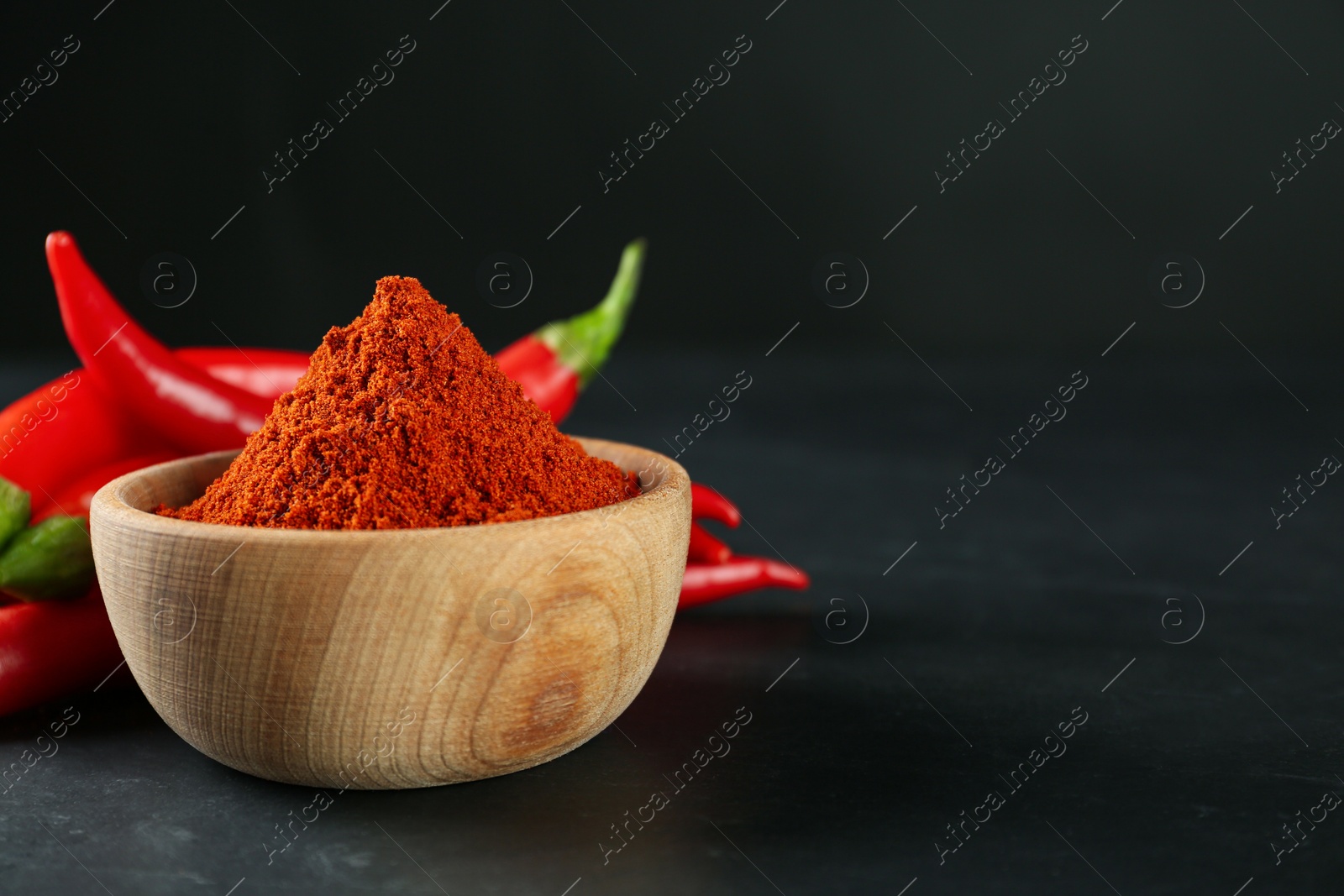 Photo of Paprika powder and fresh chili peppers on black table. Space for text