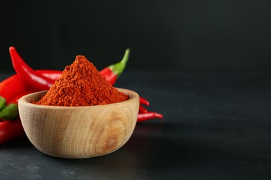 Photo of Paprika powder and fresh chili peppers on black table. Space for text