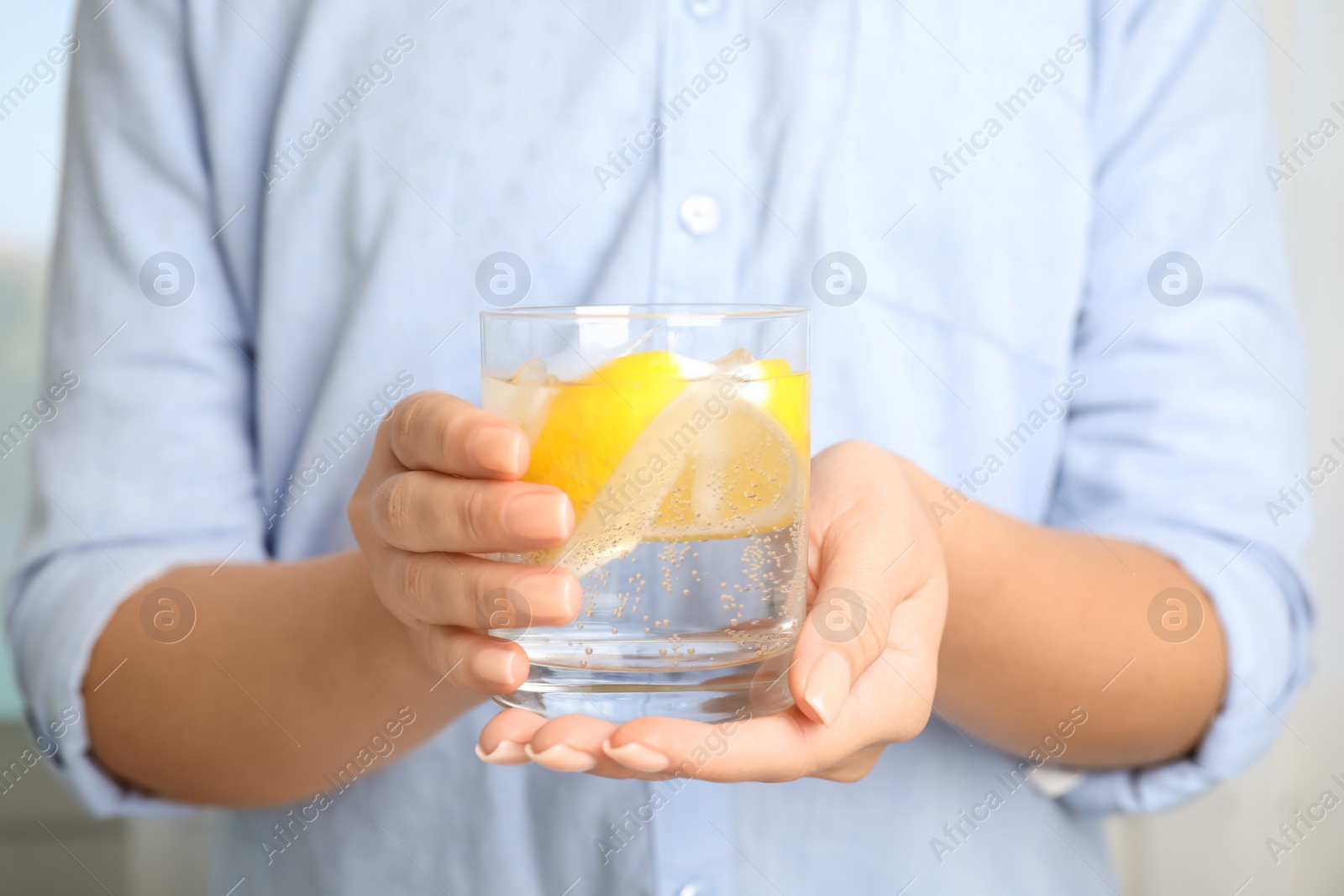 Photo of Woman holding glass of soda water with lemon slices and ice cubes, closeup