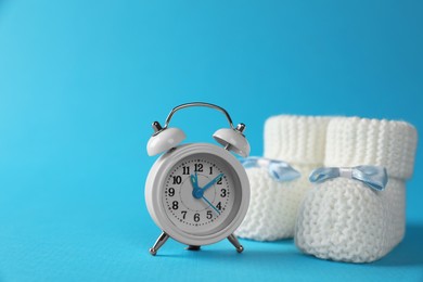 Photo of Alarm clock and baby booties on light blue background, space for text. Time to give birth