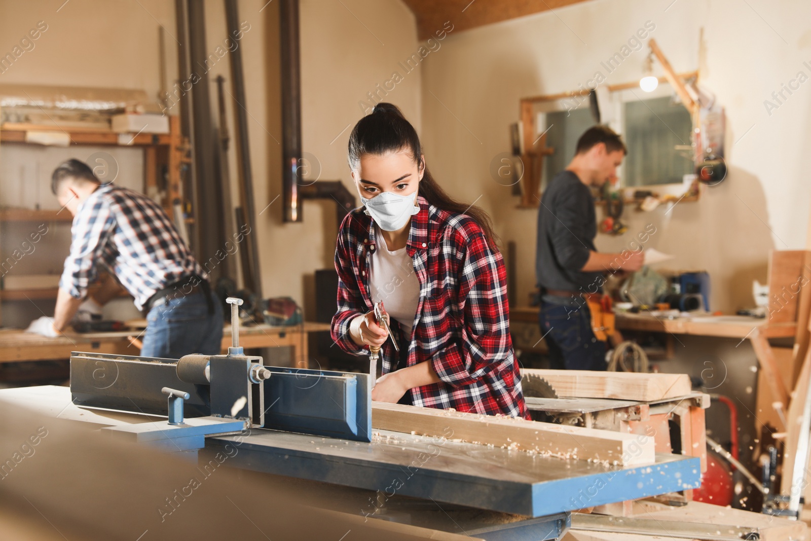 Photo of Female carpenter cleaning surface planer with air blow gun in workshop