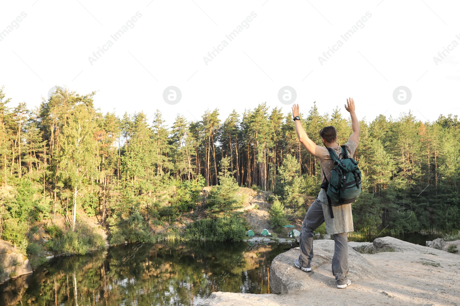 Photo of Young man on rock near lake and forest. Camping season