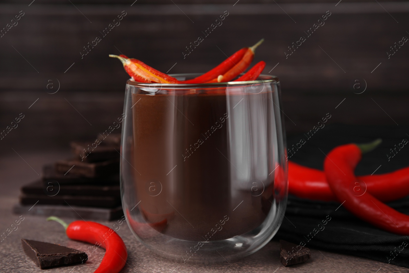 Photo of Delicious hot chocolate with chili peppers on brown textured table, closeup