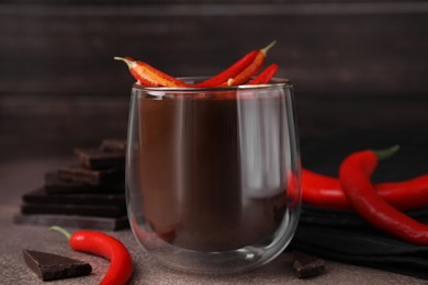 Photo of Delicious hot chocolate with chili peppers on brown textured table, closeup