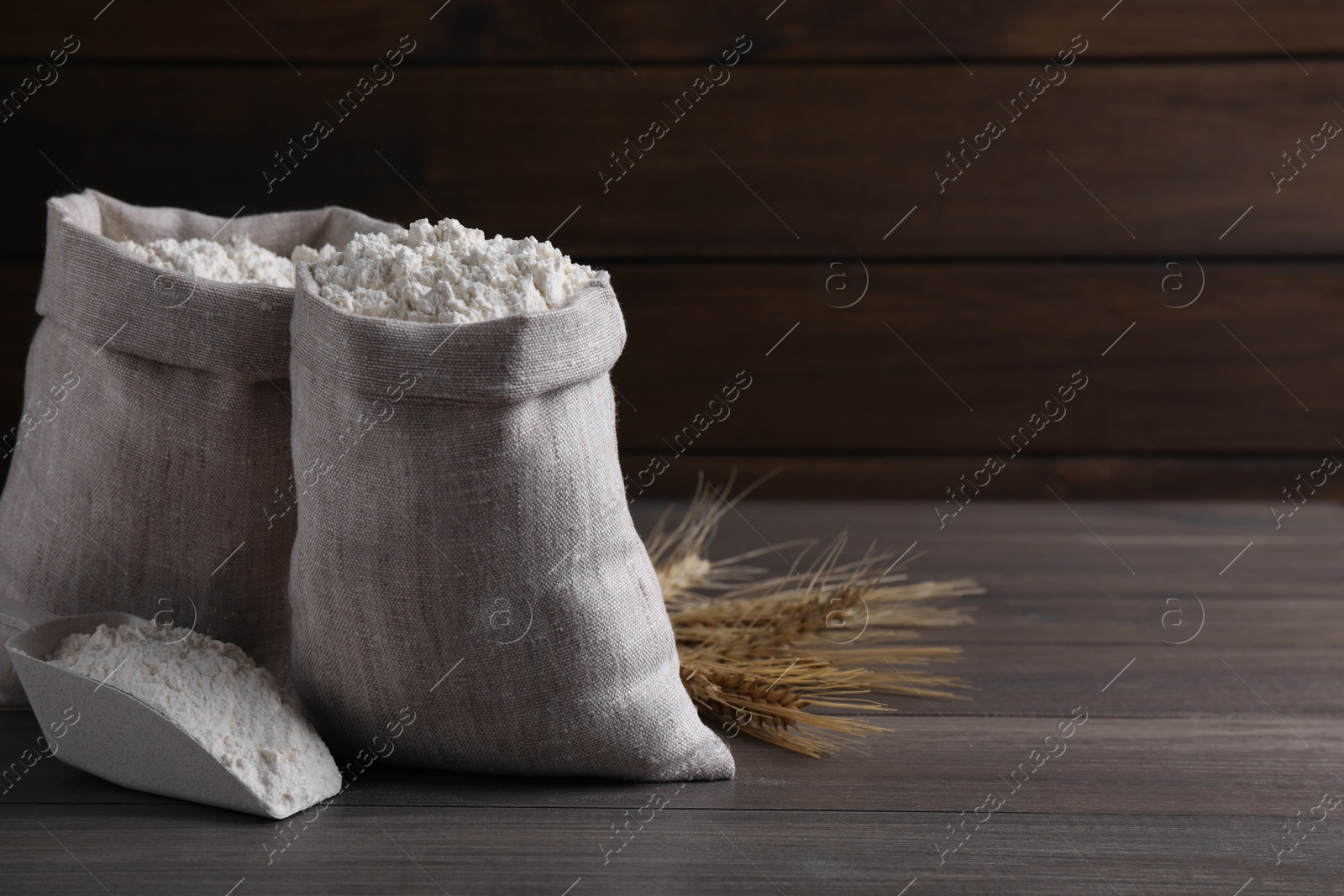 Photo of Sacks with flour and wheat spikes on wooden background. Space for text