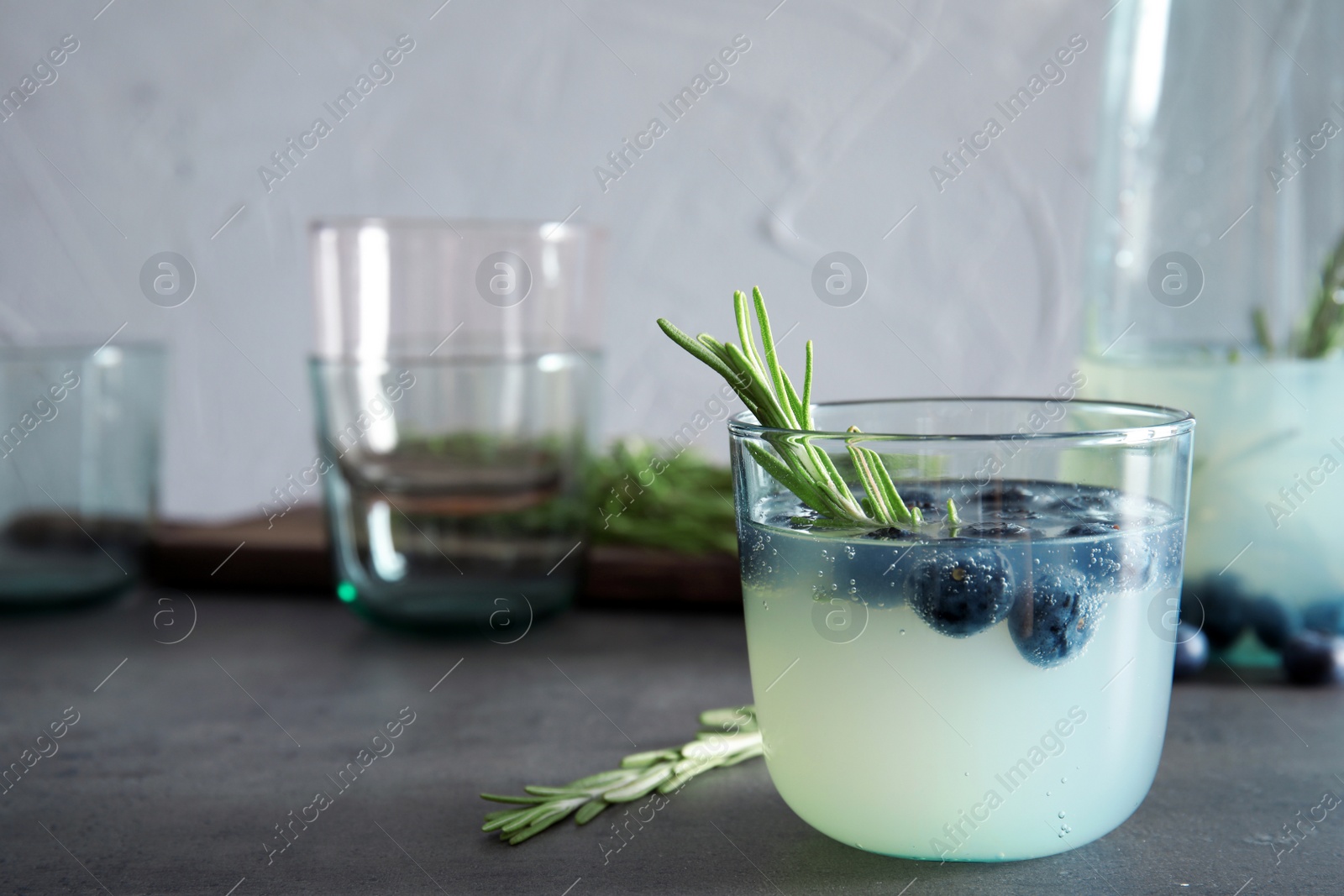 Photo of Glass of refreshing blueberry cocktail with rosemary on table