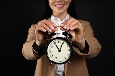Businesswoman holding alarm clock on black background, closeup. Time management