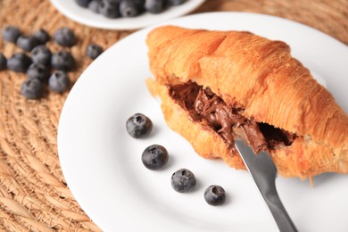 Photo of Tasty croissant with chocolate paste and blueberries on wicker mat, closeup. Space for text