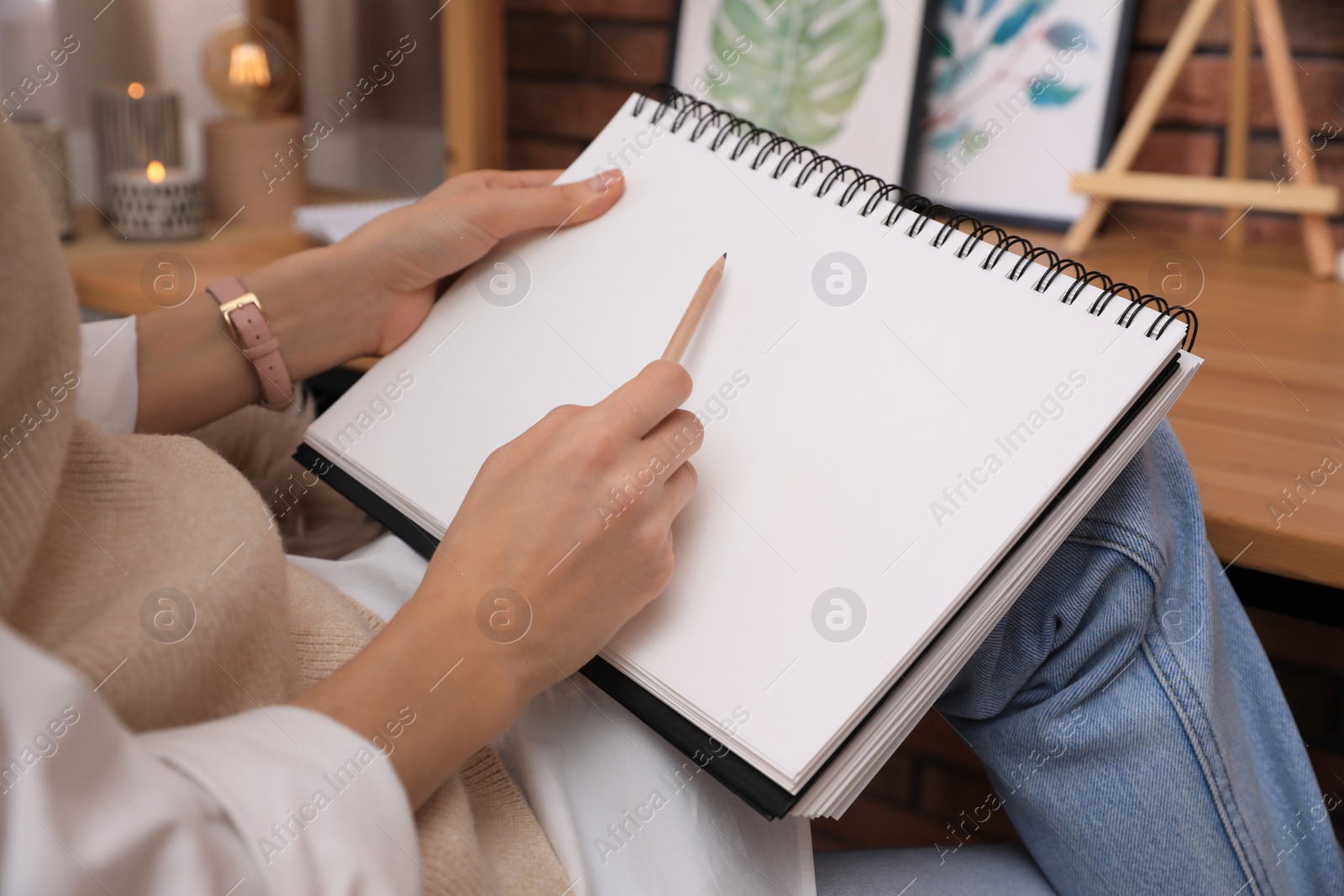 Photo of Woman drawing in sketchbook with pencil at home, closeup