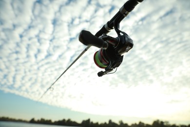 Photo of Fishing rod with reel under cloudy sky, low angle view