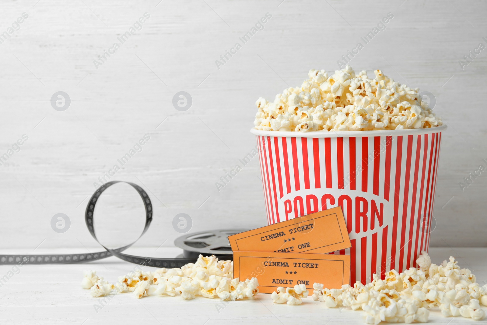 Photo of Bucket of fresh popcorn, tickets and movie reel on white wooden table, space for text. Cinema snack