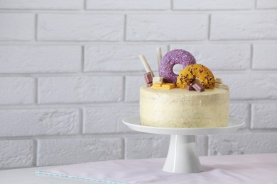 Delicious cake decorated with sweets on table near white brick wall, space for text