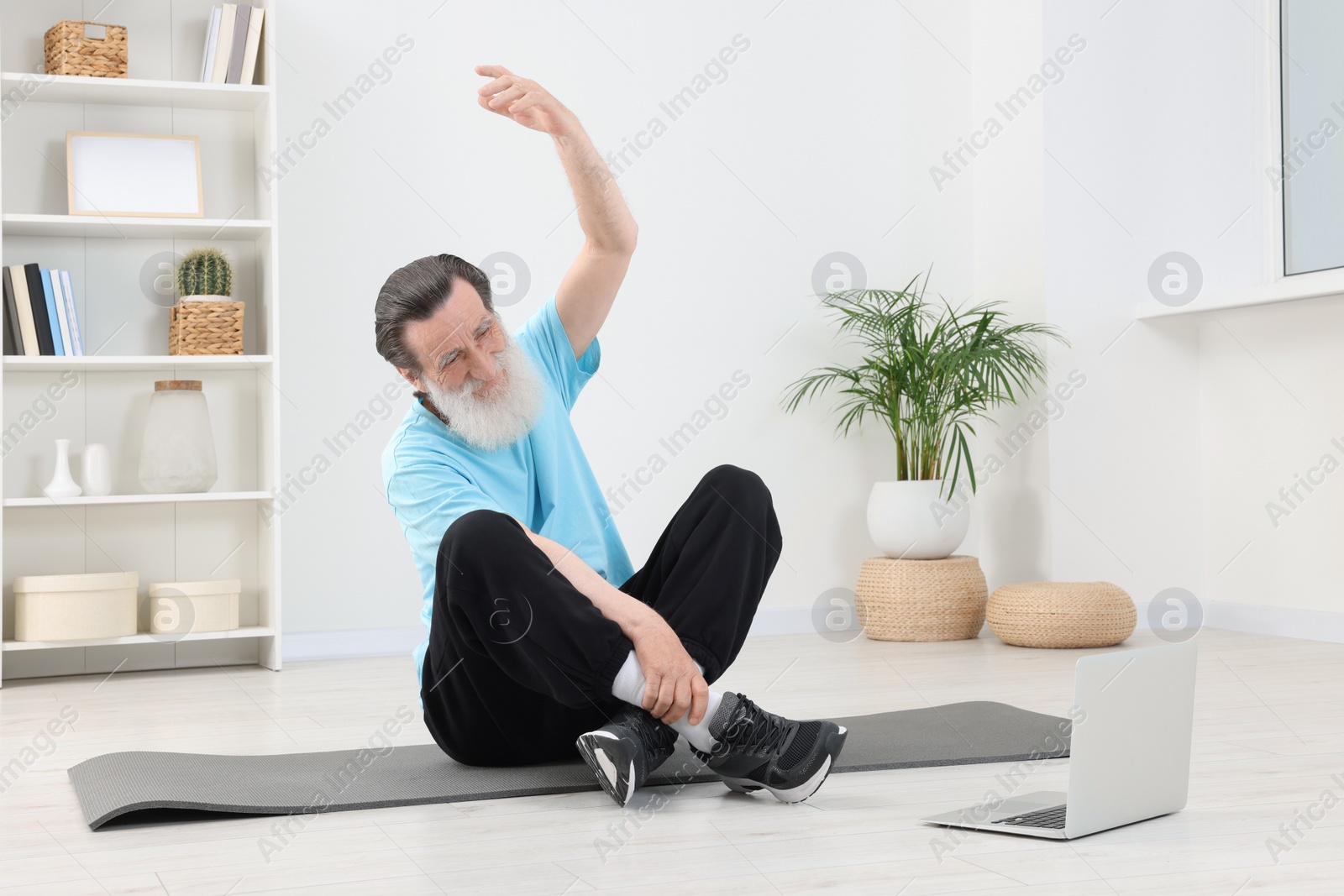 Photo of Senior man in sportswear stretching while watching online tutorial at home