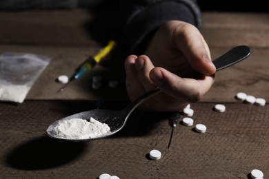 Photo of Addicted man holding spoon with drugs at wooden table, closeup