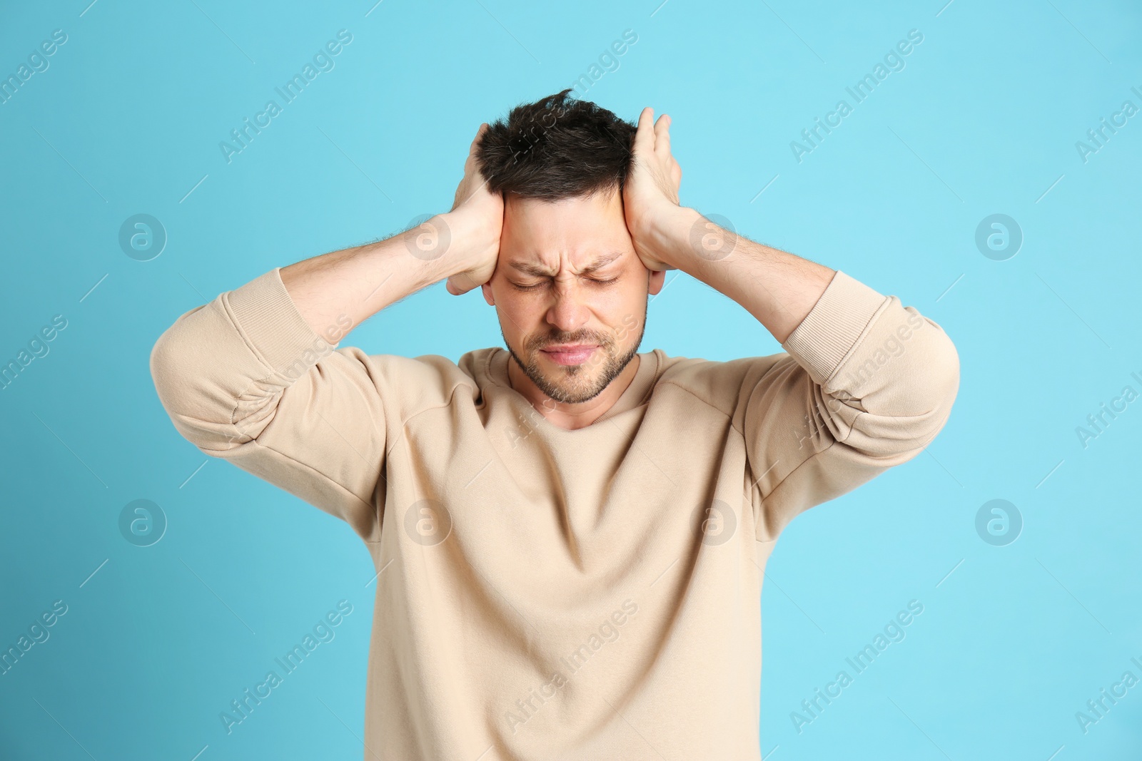 Photo of Man suffering from terrible migraine on light blue background