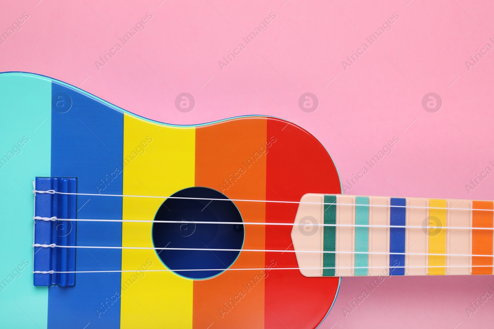 Photo of Colorful ukulele on pink background, top view. String musical instrument