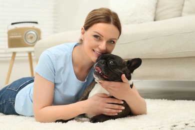 Photo of Happy woman hugging cute French Bulldog on soft carpet in room