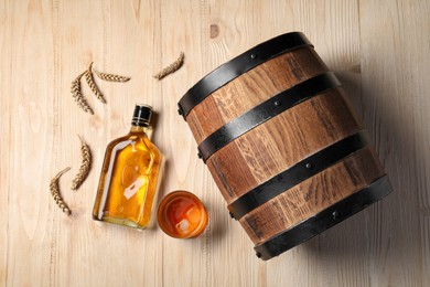 Photo of Barrel, bottle, glass of tasty whiskey and wheat spikes on wooden table, flat lay