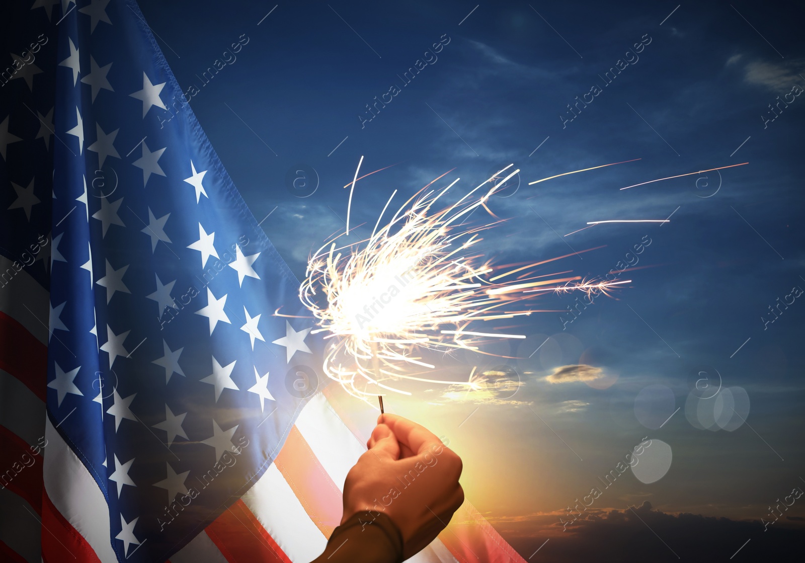 Image of 4th of July - Independence Day of USA. Woman holding burning sparkler near American flag outdoors at sunset, closeup