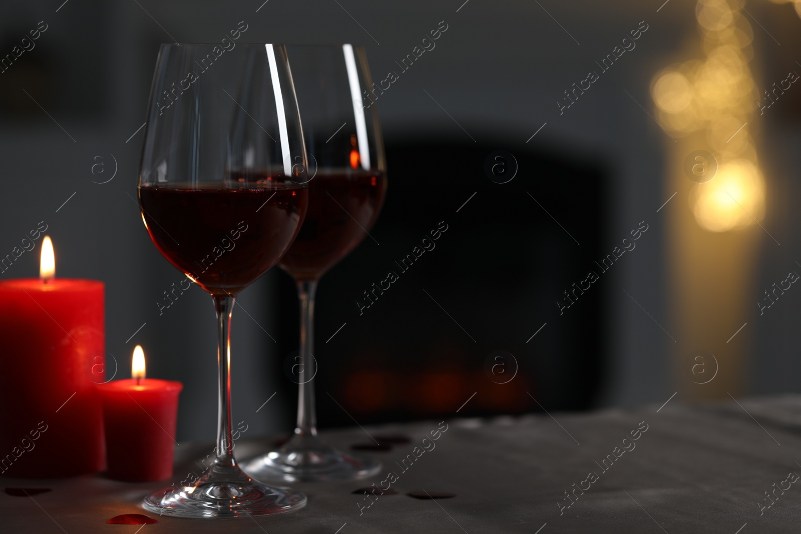 Photo of Glasses of red wine and burning candles on grey table against blurred background, space for text. Romantic atmosphere