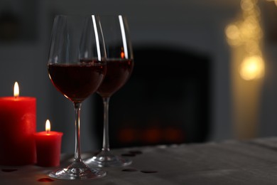 Glasses of red wine and burning candles on grey table against blurred background, space for text. Romantic atmosphere